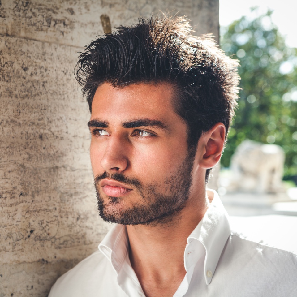 Handsome young man portrait. Intense look and eye-catching beauty. Fashionable hair and beard. The young man is wearing a white shirt.