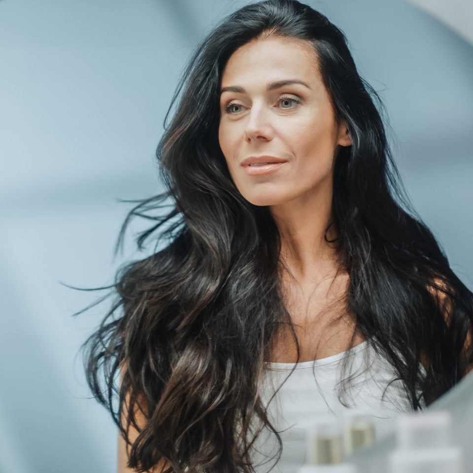 Beautiful Caucasian Middle Aged Woman Looks into Bathroom Mirror, Enjoys Her Looks. Concept for Happiness, Wellbeing, Natural Beauty and Organic Skin Care Products