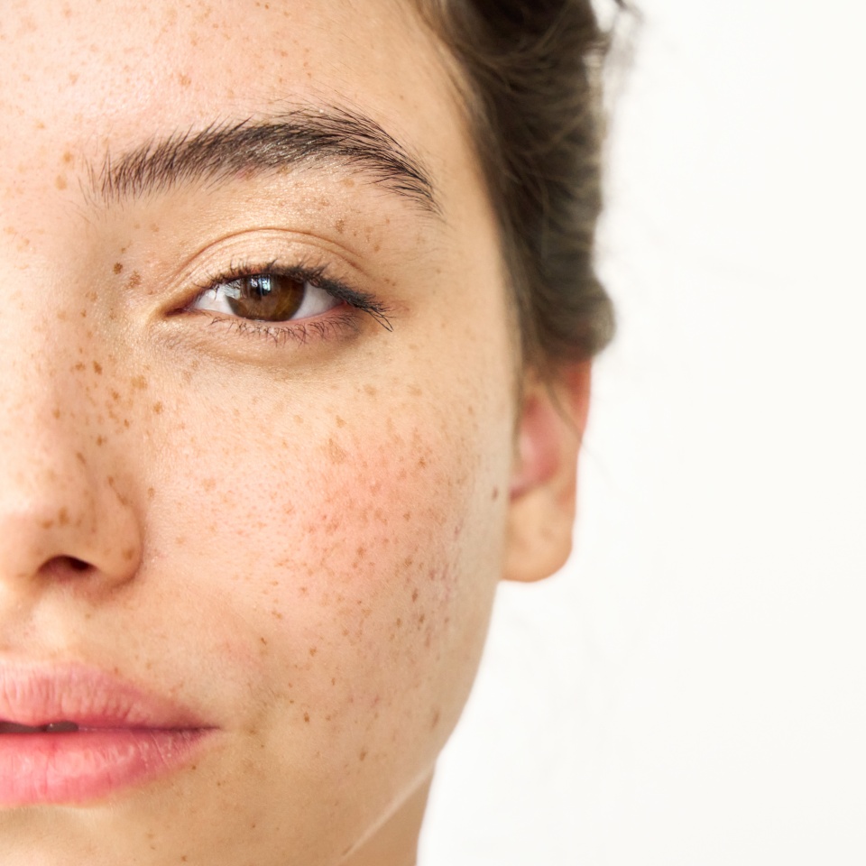 Close up aesthetic beauty half face portrait of Latin girl isolated on white background. Young adult pretty brunette Hispanic woman model with freckles looking at camera. Skincare cosmetic, skin care.