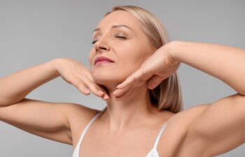 Beautiful woman touching her neck on grey background